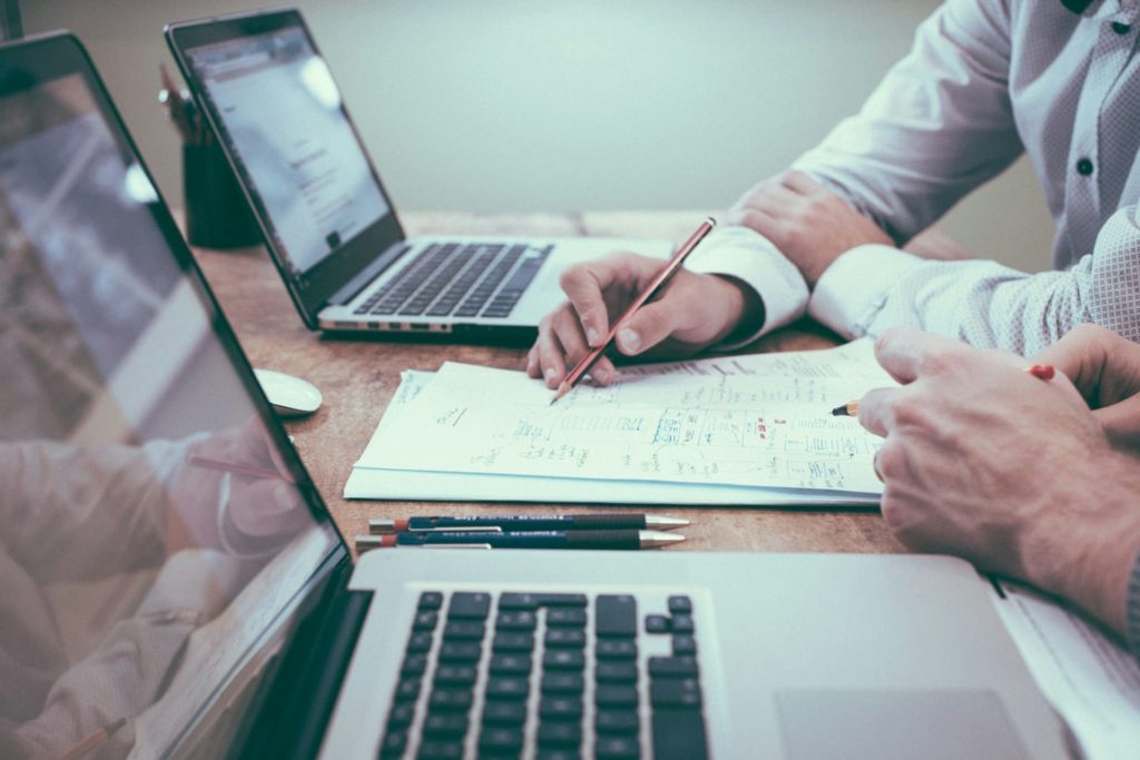 Deux ordinateurs et des mains tenant de stylos suggérant des personnes travaillant sur une réglementation ou un document