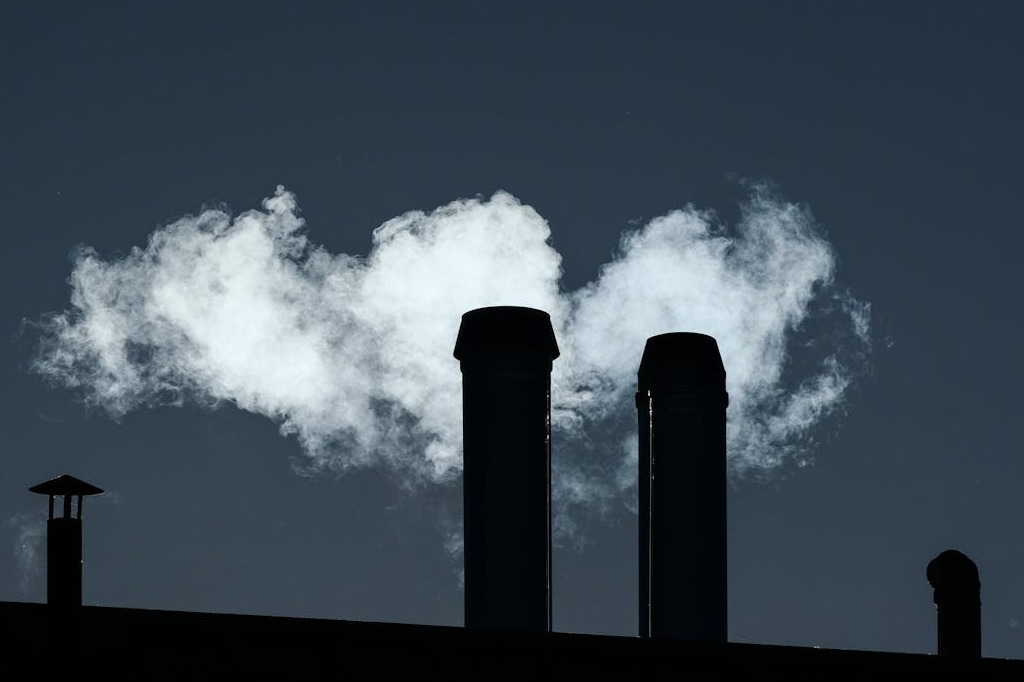 Exemple RSE : deux cheminées industrielles noires rejetant des panaches de fumée blanche dans un ciel sombre, illustrant l’impact environnemental que la RSE cherche à réduire.