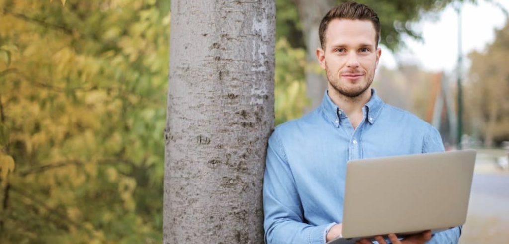 jeune homme vêtu d’une chemise et adossé à un arbre porte un ordinateur représentant le fait qu’il effectue un diagnostic rse